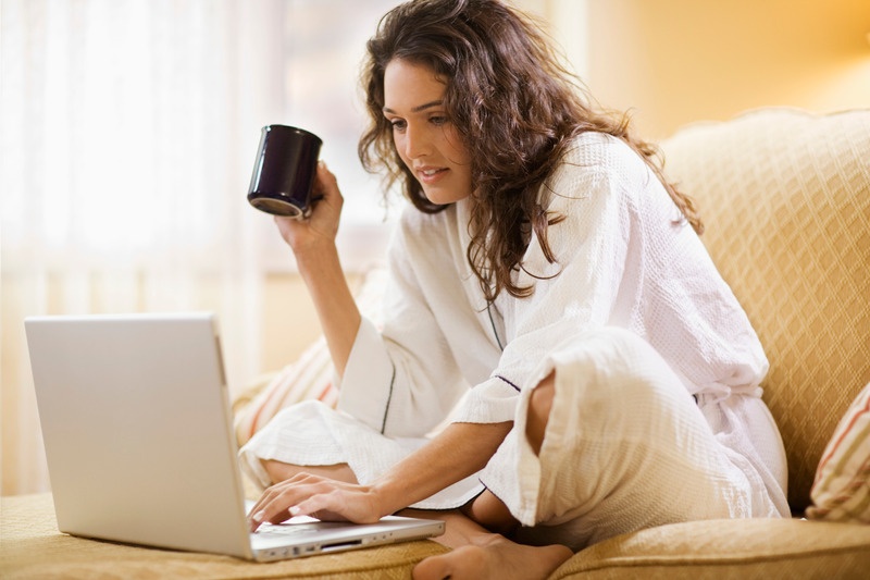 Una mujer con una taza, trabajando con su portátil en un sofá claro