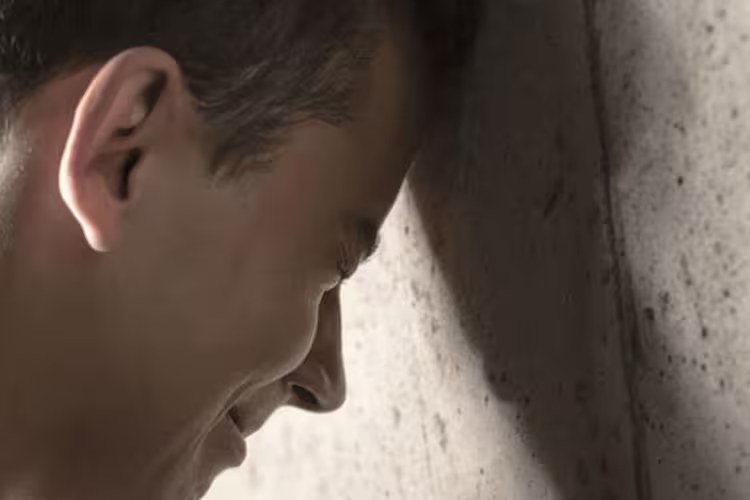 Hombre apoyado contra una pared, con la cabeza inclinada