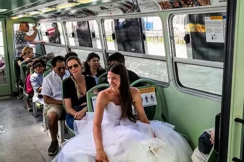 Una novia sonriendo, sentada en un autobús urbano lleno de gente
