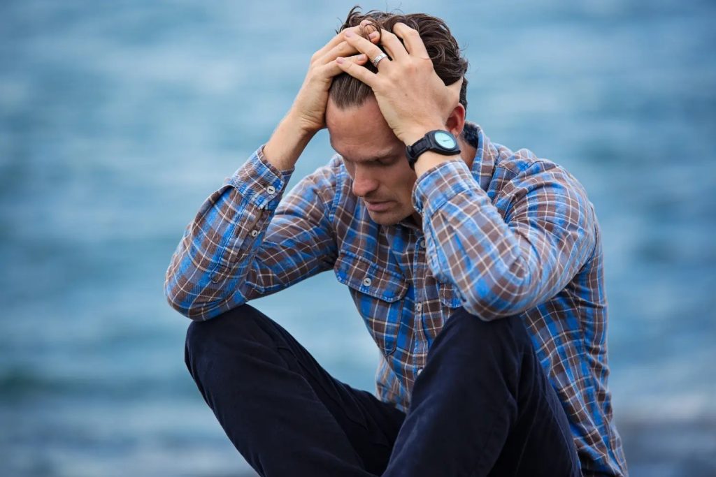 A man sitting by the water with his head in his hands