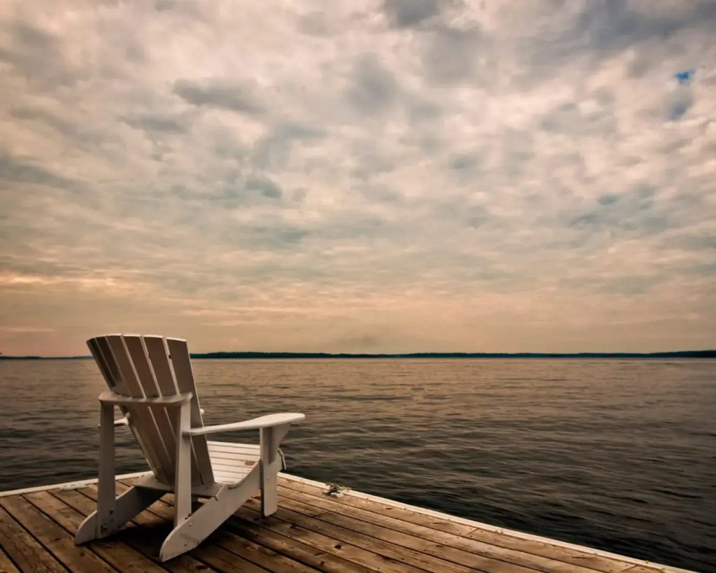 An empty chair on a wooden jetty facing the water at dusk